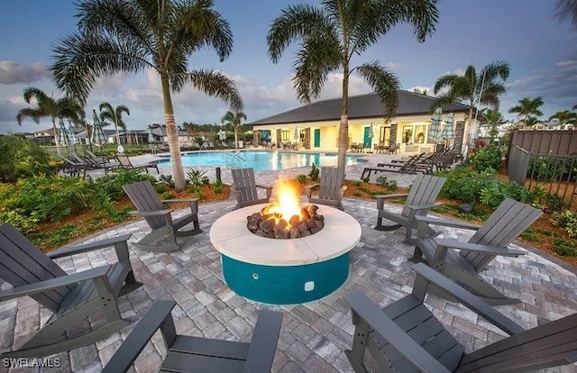 patio terrace at dusk featuring a community pool and a fire pit