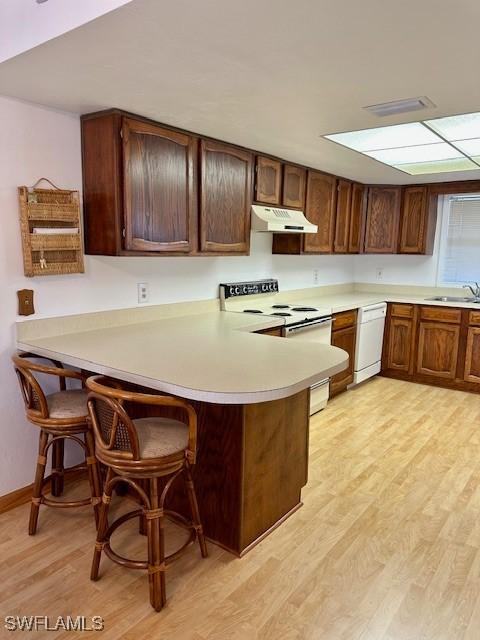 kitchen featuring sink, a breakfast bar area, kitchen peninsula, white appliances, and light hardwood / wood-style flooring