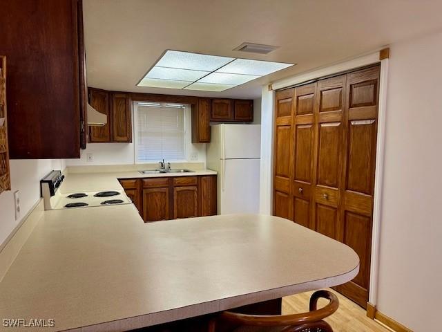 kitchen featuring sink, a kitchen breakfast bar, kitchen peninsula, white fridge, and range with electric cooktop