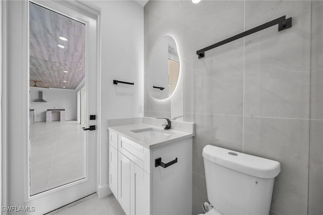 bathroom featuring toilet, vanity, and tile walls