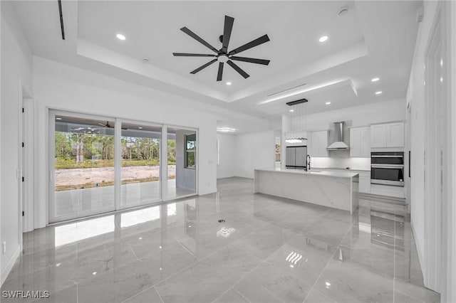 unfurnished living room with ceiling fan, a tray ceiling, and sink