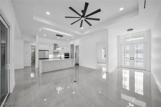 unfurnished living room featuring a raised ceiling, french doors, sink, and ceiling fan