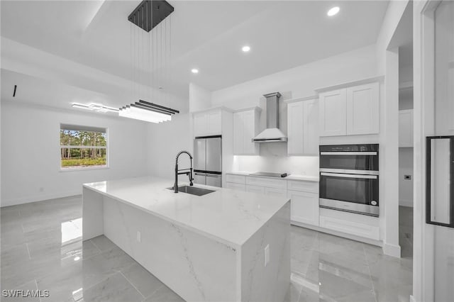 kitchen featuring appliances with stainless steel finishes, white cabinets, wall chimney exhaust hood, and an island with sink