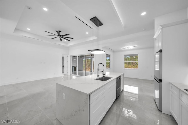 kitchen featuring light stone countertops, white cabinets, sink, a kitchen island with sink, and a tray ceiling