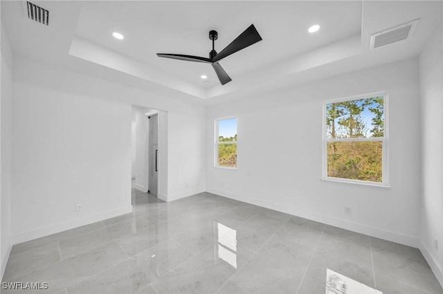 empty room with ceiling fan and a tray ceiling