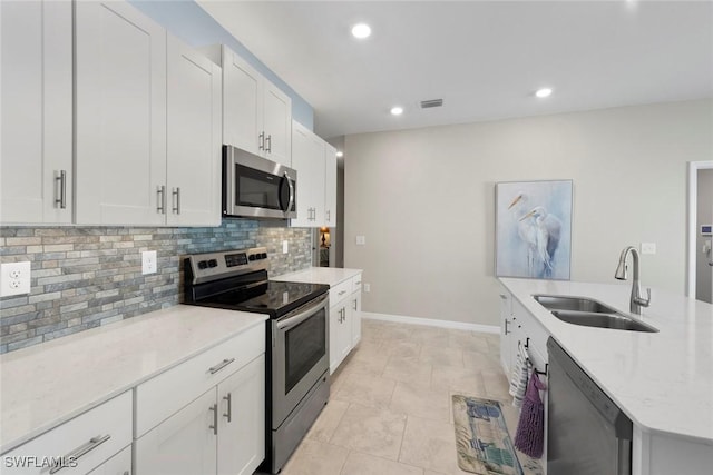 kitchen with tasteful backsplash, sink, white cabinets, light stone counters, and stainless steel appliances