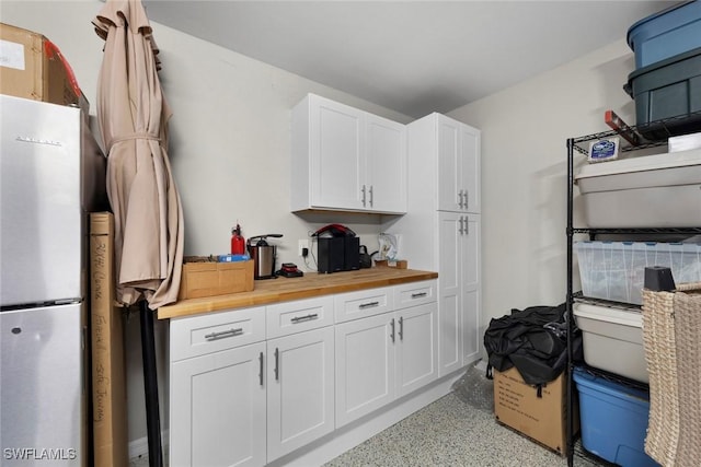 kitchen with stainless steel refrigerator, white cabinets, and wood counters