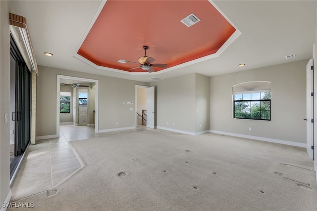 carpeted empty room with ceiling fan, plenty of natural light, and a raised ceiling