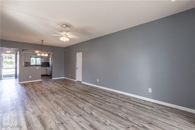 unfurnished living room featuring wood-type flooring, ceiling fan with notable chandelier, and a textured ceiling