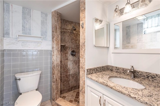 bathroom with tiled shower, vanity, toilet, and tile walls