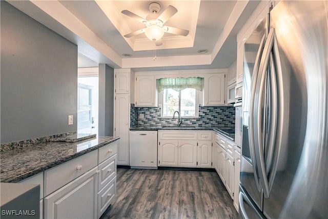 kitchen with sink, stainless steel fridge, white dishwasher, a tray ceiling, and white cabinets