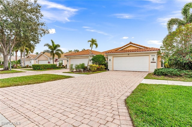 mediterranean / spanish-style house featuring a garage, a tiled roof, decorative driveway, stucco siding, and a front yard