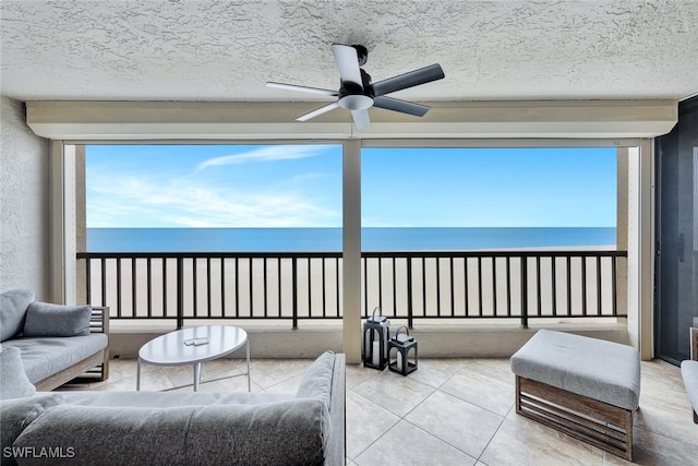 sunroom / solarium featuring a water view, ceiling fan, and a beach view