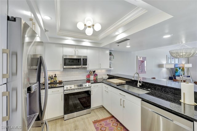 kitchen featuring light hardwood / wood-style floors, appliances with stainless steel finishes, white cabinets, sink, and a tray ceiling