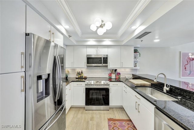 kitchen with a raised ceiling, sink, white cabinetry, dark stone counters, and stainless steel appliances