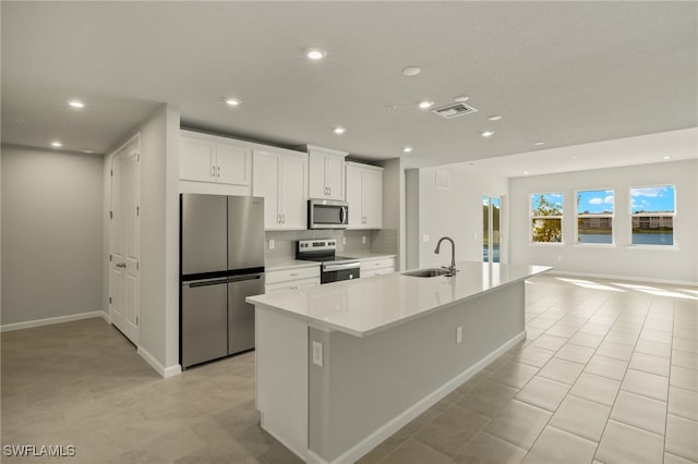 kitchen with a spacious island, a sink, decorative backsplash, stainless steel appliances, and white cabinets