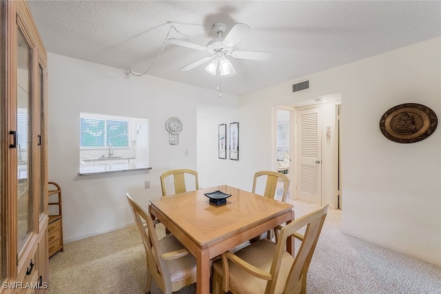 dining room with sink, light colored carpet, a textured ceiling, and ceiling fan