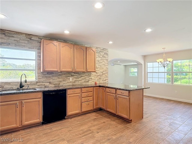 kitchen with black dishwasher, dark stone countertops, kitchen peninsula, and sink