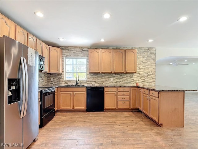 kitchen featuring backsplash, black appliances, kitchen peninsula, sink, and dark stone counters