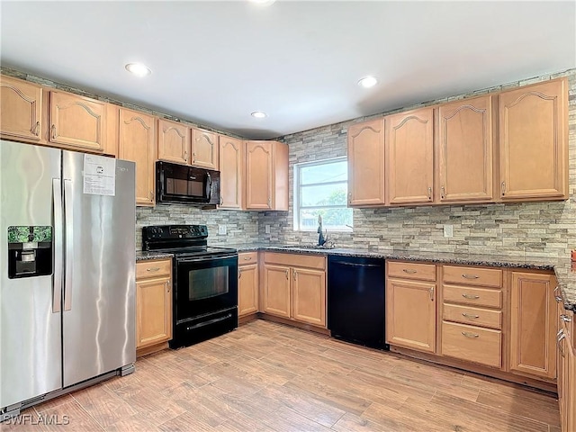 kitchen with dark stone countertops, light brown cabinetry, black appliances, light hardwood / wood-style flooring, and sink