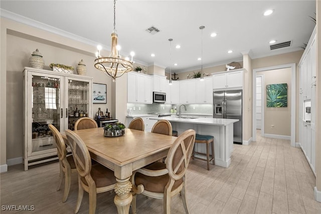 dining space with light hardwood / wood-style floors, sink, ornamental molding, and a chandelier