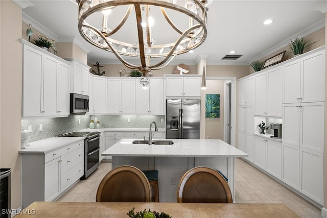 kitchen featuring decorative light fixtures, a center island with sink, sink, crown molding, and appliances with stainless steel finishes