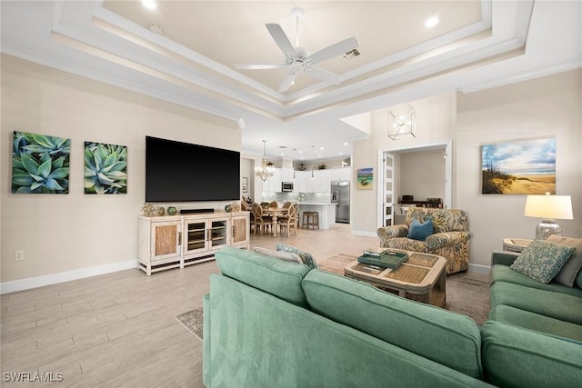 living room with ceiling fan with notable chandelier, a tray ceiling, and ornamental molding