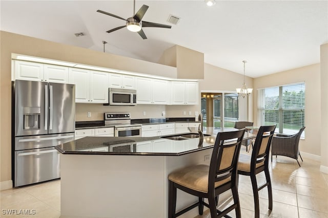 kitchen featuring white cabinets, lofted ceiling, decorative light fixtures, stainless steel appliances, and an island with sink