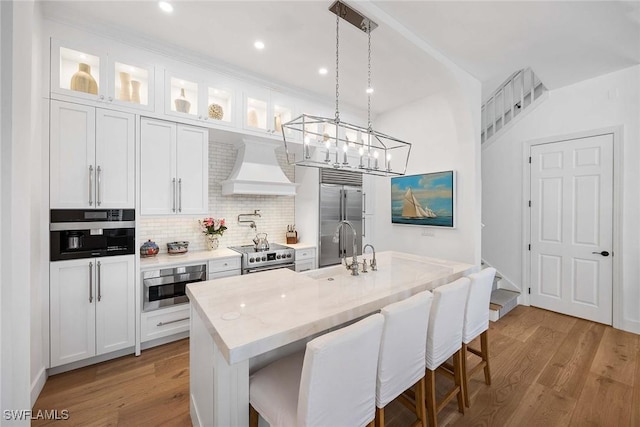 kitchen featuring white cabinetry, a center island with sink, custom range hood, and stainless steel appliances