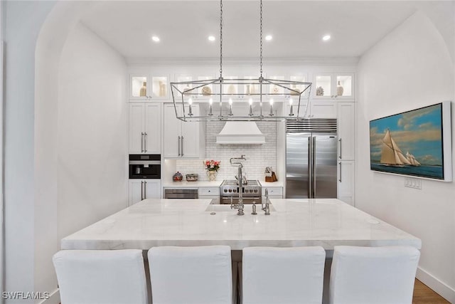 kitchen featuring white cabinetry, custom exhaust hood, light stone counters, and stainless steel built in refrigerator