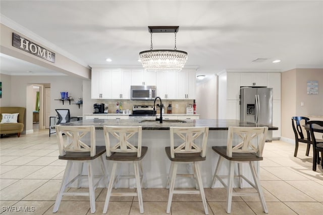 kitchen with appliances with stainless steel finishes, an island with sink, backsplash, white cabinets, and light stone counters