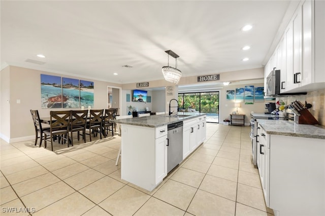 kitchen with light stone counters, decorative light fixtures, stainless steel appliances, and an island with sink