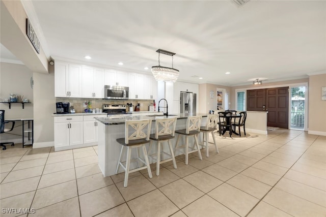 kitchen with sink, appliances with stainless steel finishes, white cabinetry, a center island with sink, and decorative light fixtures