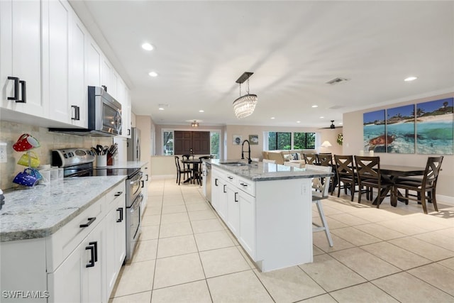 kitchen featuring white cabinetry, a center island with sink, pendant lighting, stainless steel appliances, and light stone countertops