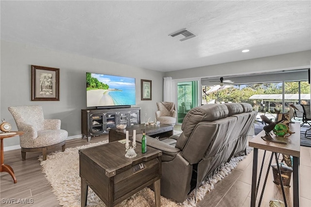 living room with a textured ceiling, ceiling fan, and light hardwood / wood-style flooring