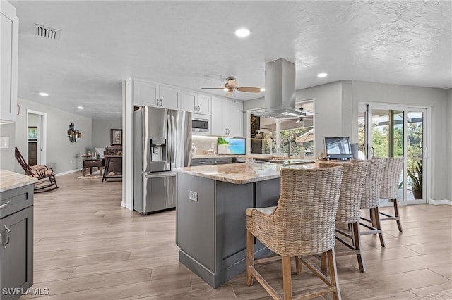 kitchen with white cabinetry, island exhaust hood, stainless steel appliances, light stone counters, and a breakfast bar