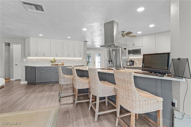 kitchen with a breakfast bar, gray cabinetry, stainless steel appliances, white cabinets, and island range hood