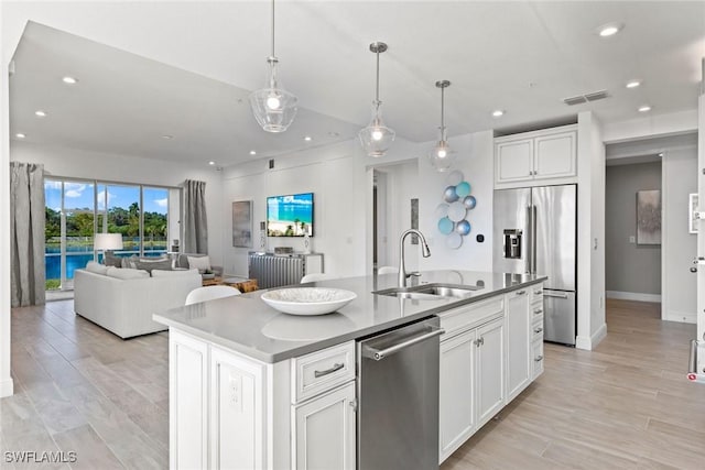 kitchen featuring pendant lighting, appliances with stainless steel finishes, white cabinetry, sink, and a kitchen island with sink