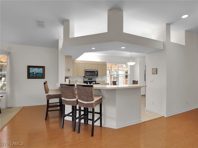 kitchen featuring appliances with stainless steel finishes, kitchen peninsula, light hardwood / wood-style floors, and a breakfast bar area