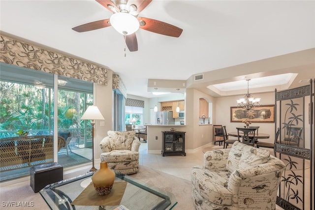 living room with ceiling fan with notable chandelier, light tile patterned floors, and a tray ceiling