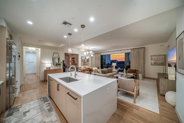 kitchen with pendant lighting, an inviting chandelier, light hardwood / wood-style floors, sink, and an island with sink