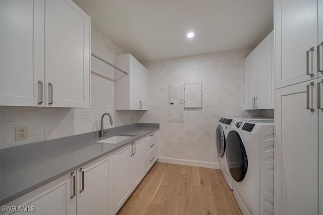 washroom with washer and dryer, sink, light hardwood / wood-style flooring, and cabinets