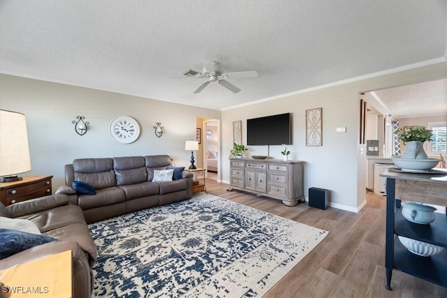 living room featuring ceiling fan, ornamental molding, a textured ceiling, and light wood-type flooring