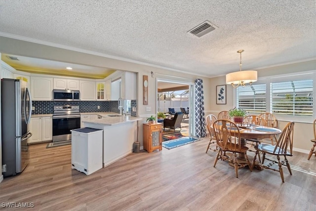 kitchen featuring pendant lighting, stainless steel appliances, white cabinets, kitchen peninsula, and light wood-type flooring