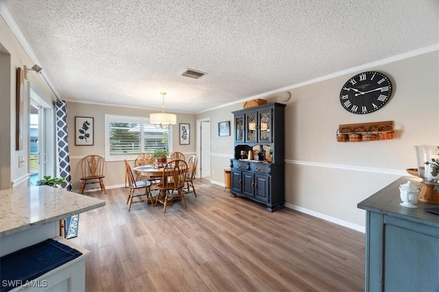 dining room featuring wood-type flooring, ornamental molding, and a textured ceiling