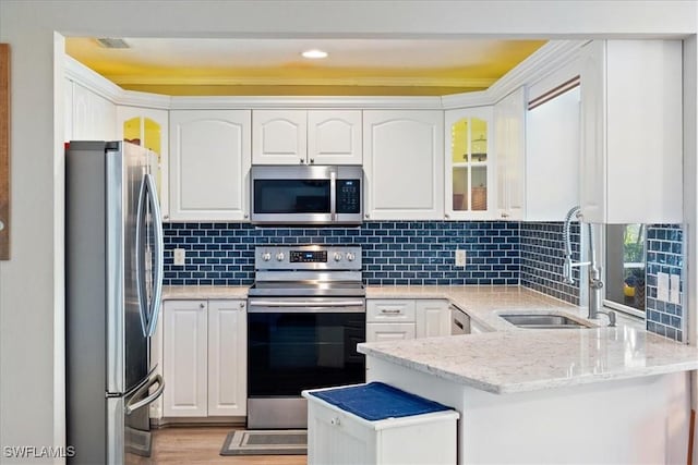 kitchen featuring appliances with stainless steel finishes, white cabinetry, sink, backsplash, and light stone counters