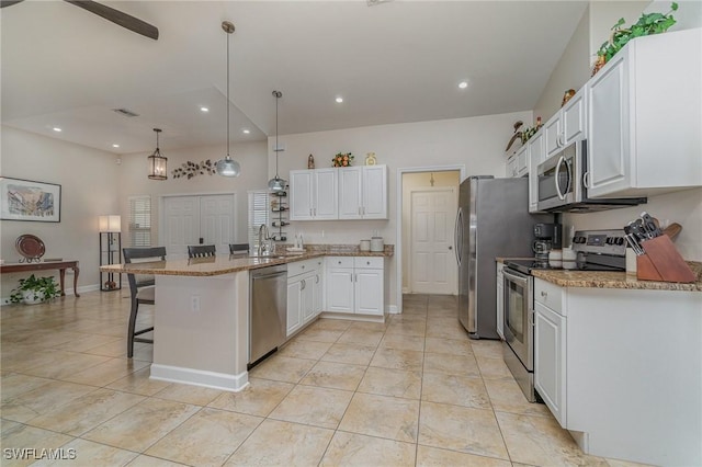 kitchen featuring a kitchen bar, hanging light fixtures, stainless steel appliances, white cabinets, and light stone counters