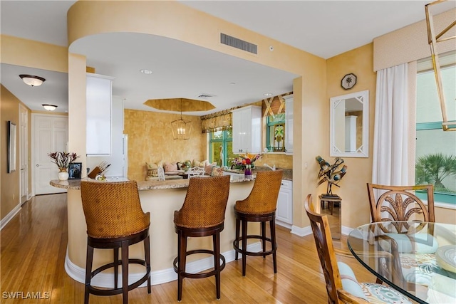 interior space with kitchen peninsula, light hardwood / wood-style floors, white cabinets, and light stone countertops