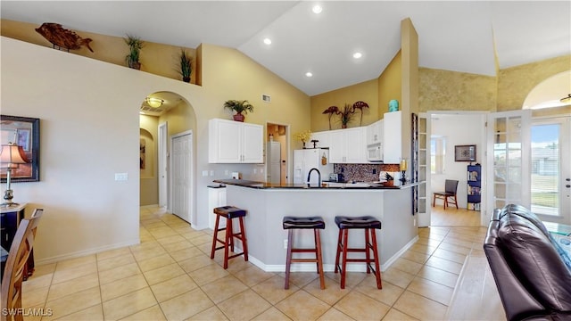 kitchen with dark countertops, white appliances, arched walkways, and a breakfast bar area