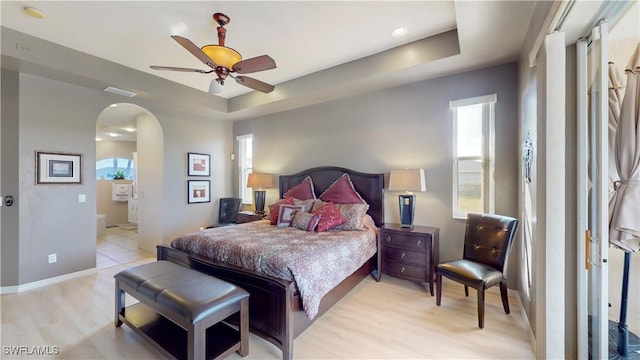 bedroom with baseboards, visible vents, arched walkways, a tray ceiling, and light wood-type flooring